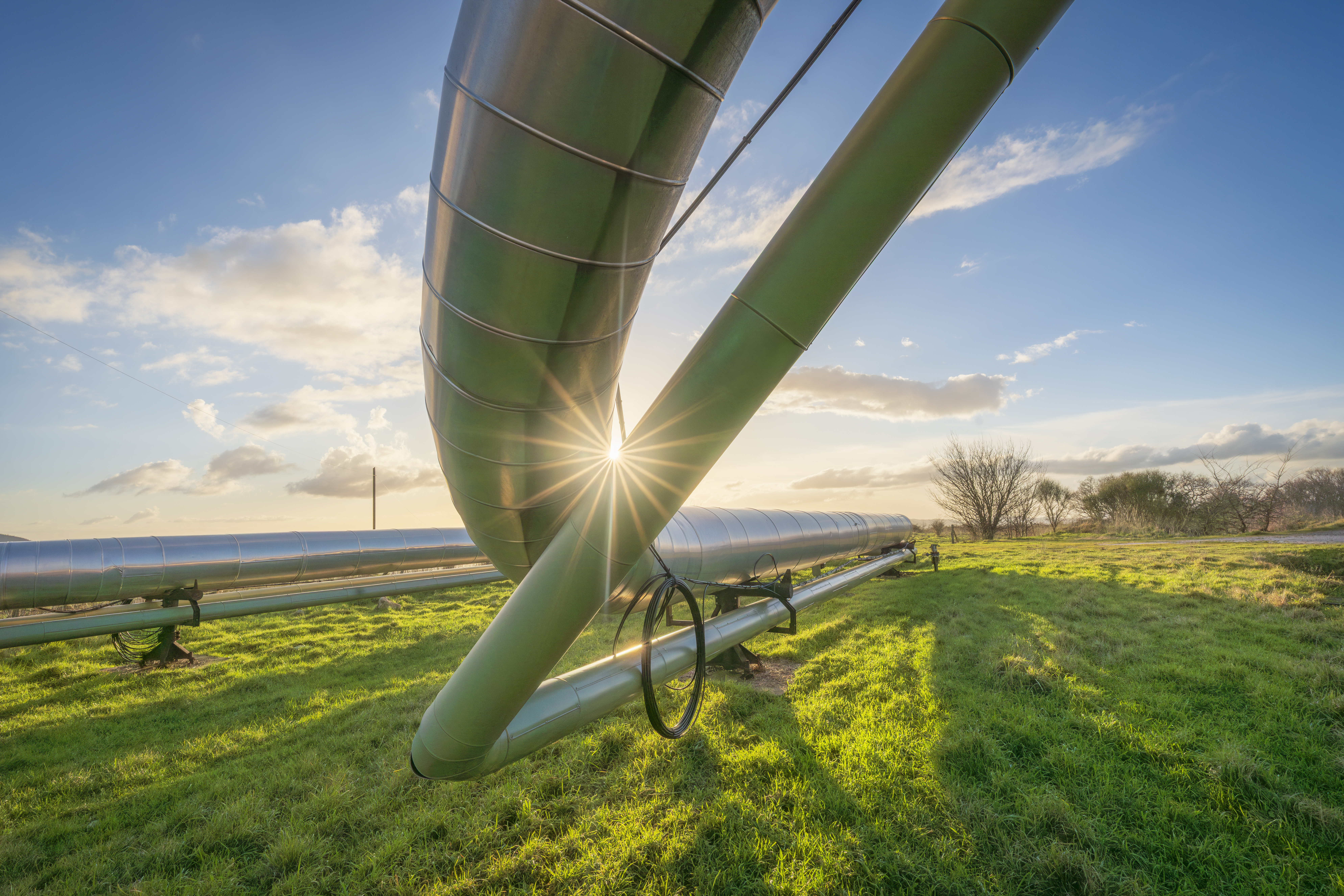 Geothermal energy pipelines crossing a green field at sunset